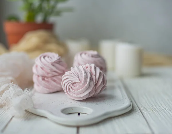 Zelfgemaakte marshmallow Zephyr op een witte plaat met kaarsen en kamer boom op een lichte houten tafel. Roze zoete zelfgemaakte marshmallow. Kleurrijke meringues op een witte achtergrond. Dessert — Stockfoto