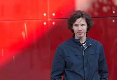 Kızıl duvarın yanında gölgesi olan genç bir adam.