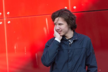 Kızıl duvarın yanında gölgesi olan genç bir adam.