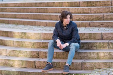 Genç adam merdivenlerde oturuyor ve bir şey bekliyor.