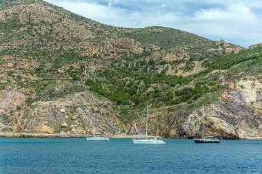 İspanya 'nın Cartagena kenti yakınlarındaki bir körfezde, dağlık bir kıyıda iki beyaz ve bir siyah yat.