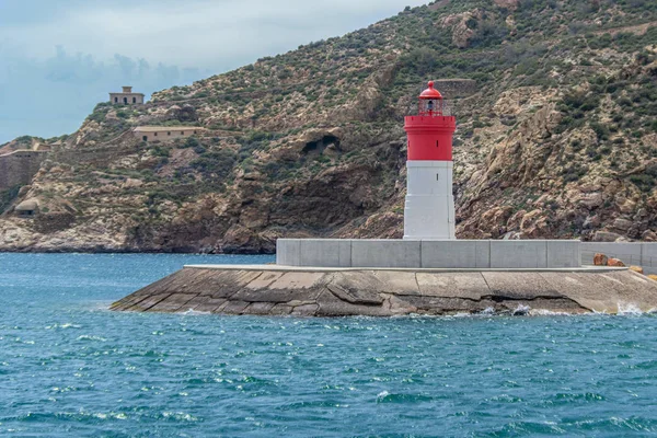 İspanya, Cartagena 'daki dağların arka planına karşı denizdeki kırmızı ve beyaz deniz feneri.