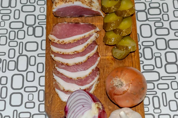 Viande salée tranchée sur une planche de bois avec des concombres salés — Photo