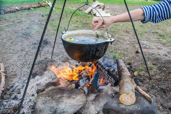 fish soup cooking in a pot on a fire in the forest by the sea