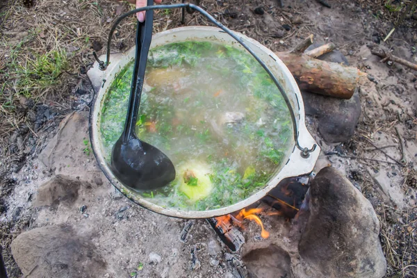 fish soup cooking in a pot on a fire in the forest by the sea