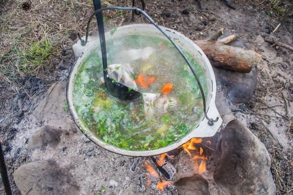 fish soup cooking in a pot on a fire in the forest by the sea