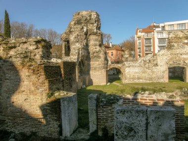 Kemerler ve sütunlarla modern evler ve mavi gökyüzü arka planı zemin seviyesinin altında Antik bir taş yapı kalıntıları