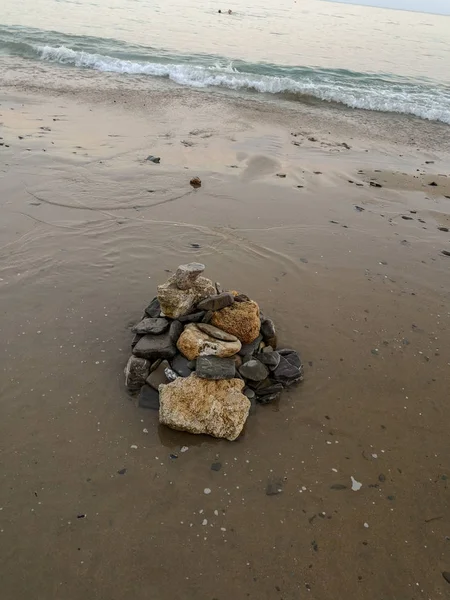 Beyaz köpük mavi dalgalar tarafından yıkanmış ıslak kum üzerinde taş kompozisyonu