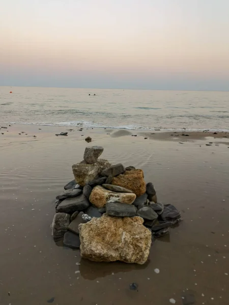 Gelen dalgalar arka planda ıslak kum yığını üzerinde yığılmış farklı boyutlarda koyu ve hafif taşlar