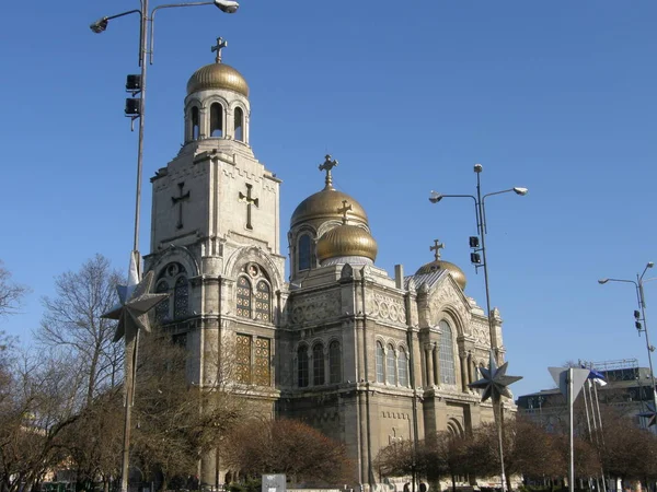 Mavi gökyüzü ve çıplak ağaçlara karşı çan kulesinde altın kubbeler ve vitray pencereli antik taş kilise