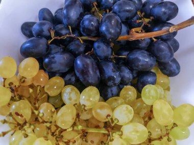 Beyaz bir tabakta bir avuç siyah ve sarı üzüm