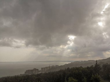 Gri bulutların içinden geçen güneş ışınları ve orman ve denizle büyümüş dağın üzerinden gelen yağmur akıntıları