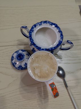 Süt ve köpüklü bir kupa dolusu baykuş şekerli ve çay kaşığıyla beyaz bir tahta masanın üzerinde duruyor.