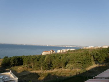 Sahil boyunca binaları olan deniz koyunun üst manzarası ve aşağı inen dağ yeşil ağaçlarla kaplı.