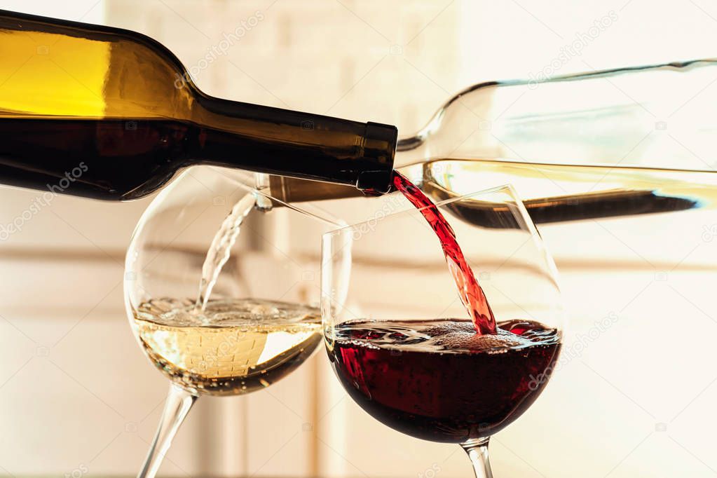 Pouring delicious wine into glasses on light background