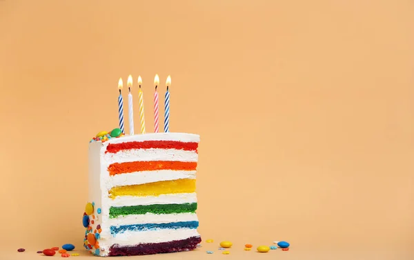Slice of delicious rainbow cake with candles on color background