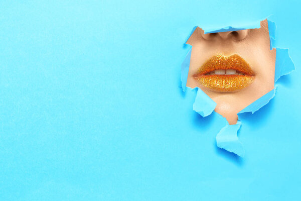 View of beautiful young woman with creative lips makeup through hole in color paper
