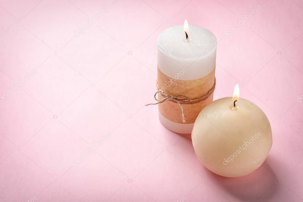 Burning wax candles of different shapes on color background