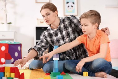 Young woman and little boy with autistic disorder playing at home clipart