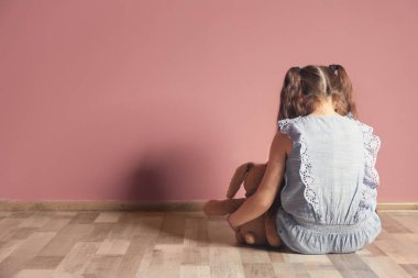 Boş odada renk duvarının yakınında katta oturan oyuncak olan küçük kız. Otizm kavramı