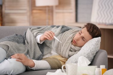 Soğuk evde kanepe üzerinde acı termometre ile hasta genç adam