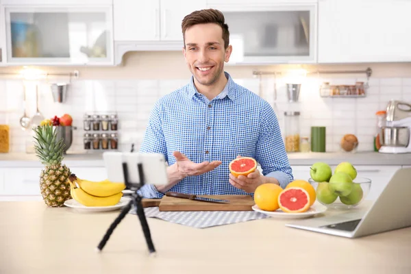 Young blogger with fruits recording video in kitchen