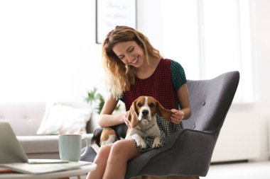 Köpeğini evde koltukta oturan genç kadınla