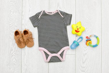 Tahta arka planda bebek kıyafetleri ve aksesuarları olan düz kompozisyon.