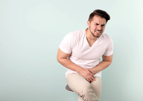 Young man with urological problems suffering from pain on color background