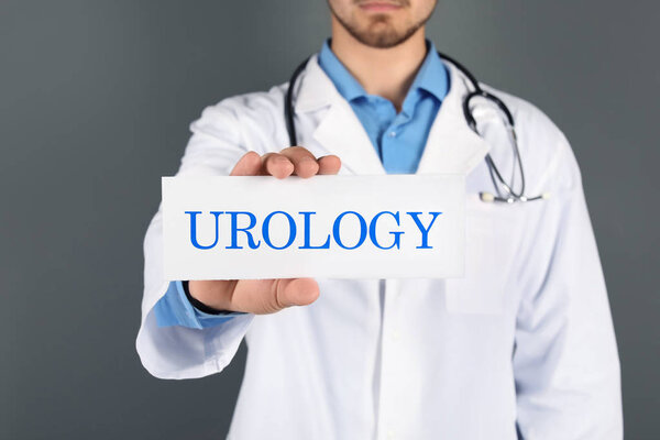 Male doctor holding paper with word UROLOGY on grey background