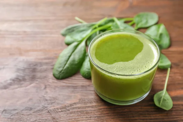 Glass with delicious detox juice and spinach on wooden background