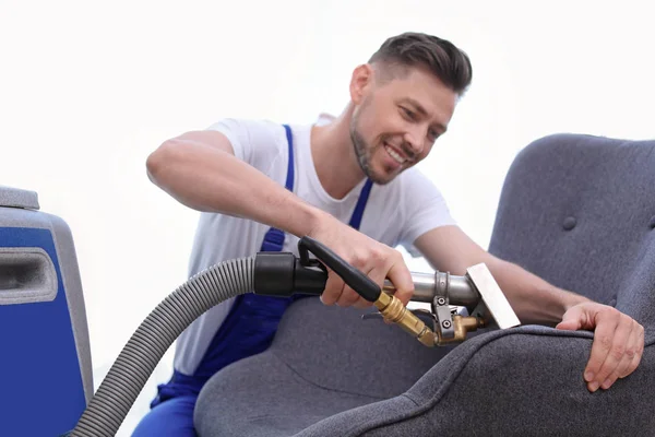 Dry cleaning worker removing dirt from armchair indoors