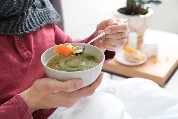 自宅のベッドで風邪を治す病気の若い男を食べるスープ — ストック写真