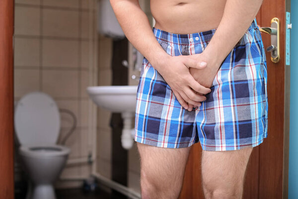 Young man with urological problems suffering from pain near toilet