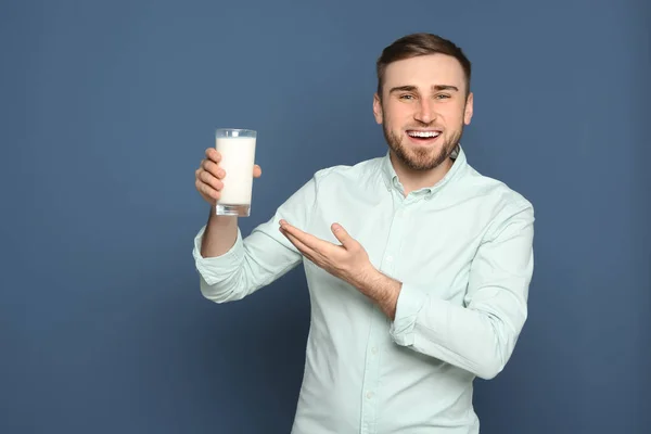 Young man with glass of tasty milk on color background