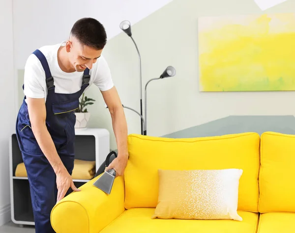 Dry cleaning worker removing dirt from sofa indoors