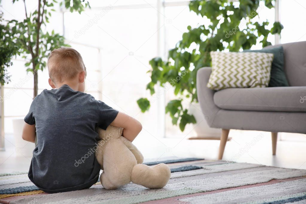 Lonely little boy with teddy bear sitting on floor at home. Autism concept