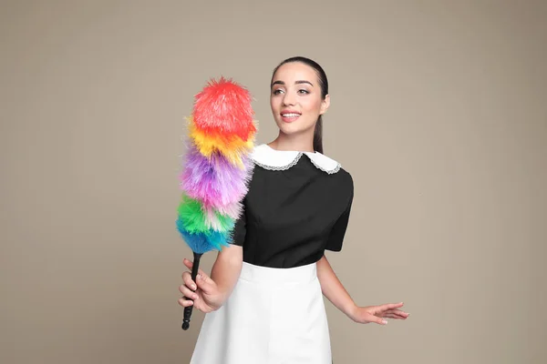 Young chambermaid with dusting brush on color background