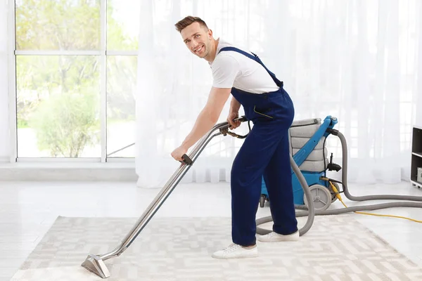 Male worker removing dirt from carpet with professional vacuum cleaner indoors