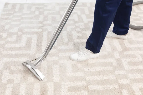 Male worker removing dirt from carpet with professional vacuum cleaner indoors