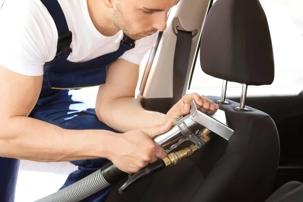 Male worker removing dirt from car seat with professional vacuum cleaner