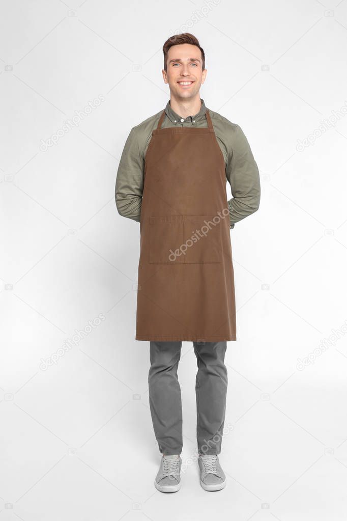 Full length portrait of handsome waiter in apron on light background