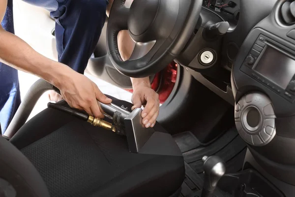 Male worker removing dirt from car seat with professional vacuum cleaner