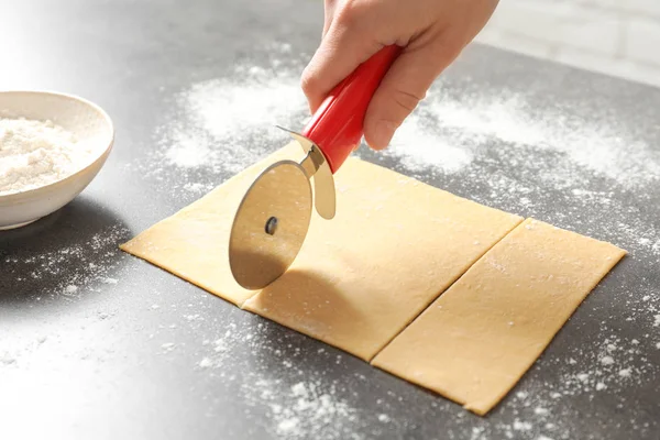 Young woman cutting dough for pasta on table