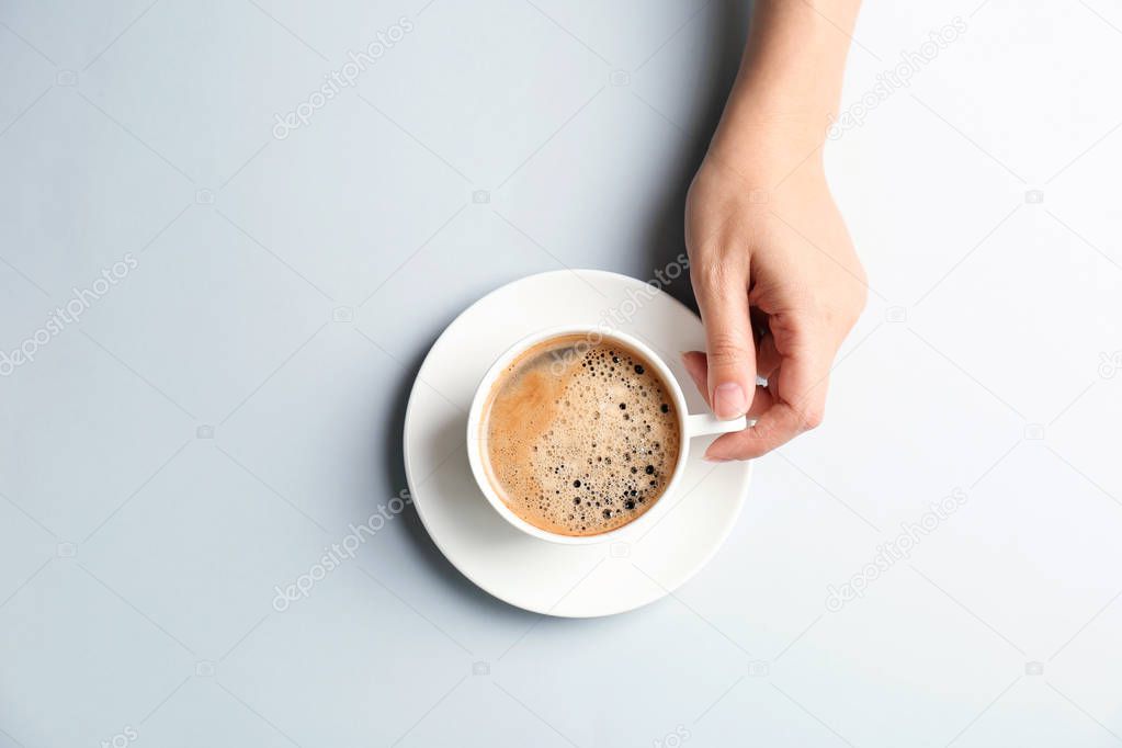 Young woman with cup of delicious hot coffee on light background, top view