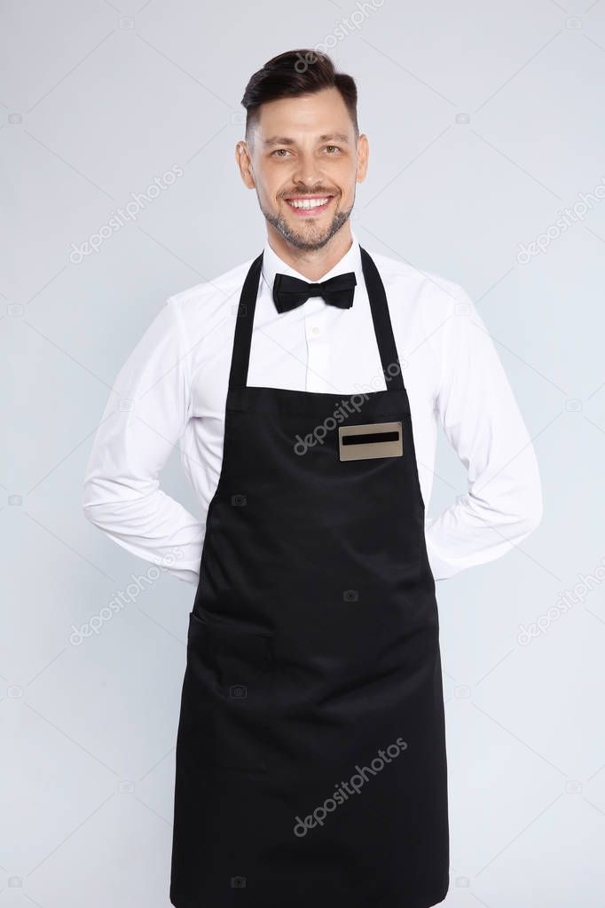 Portrait of handsome waiter in elegant uniform on light background