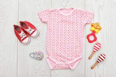 Tahta arka planda bebek kıyafetleri ve aksesuarları olan düz kompozisyon.