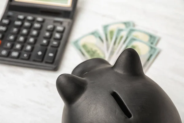 Black piggy bank near money and calculator on table