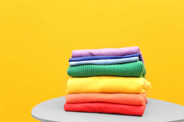 Stack of rainbow clothes on table against color background