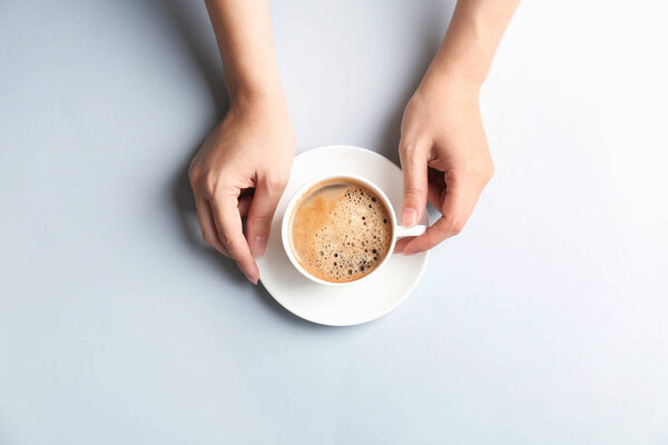Young woman with cup of delicious hot coffee on light background, top view